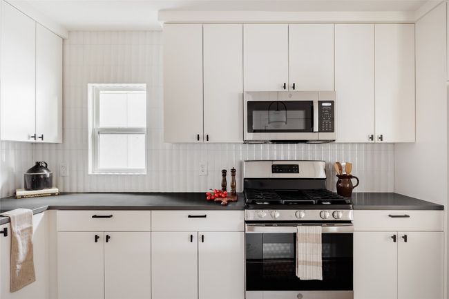 Kitchen with stainless steel appliances, white cabinets, backsplash, and dark countertops | Image 14