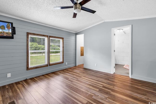 Spare room featuring a ceiling fan, a textured ceiling, vaulted ceiling, wood finished floors, and wood walls | Image 12