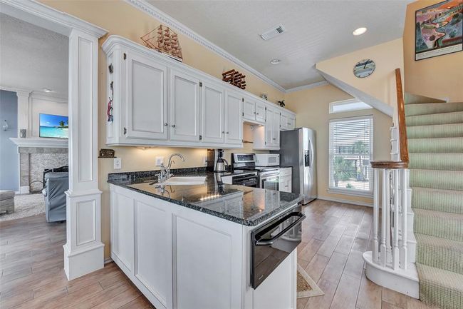 Crisp white cabinets contrast beautifully with sleek granite countertops, offering both style and storage. This well-planned layout is perfect for cooking, serving, and staying connected to the main living space. | Image 12