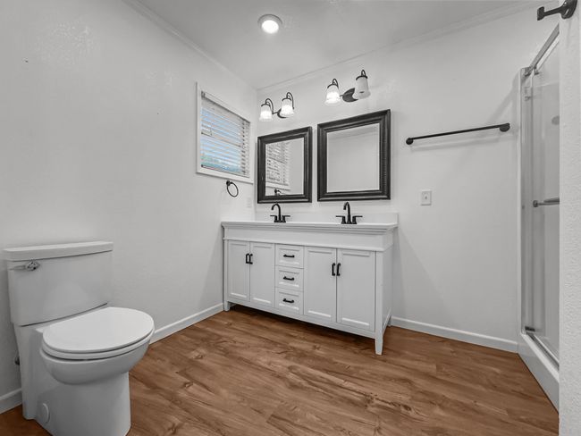 Bathroom featuring double vanity, a shower with shower door, wood finished floors, and ornamental molding | Image 11