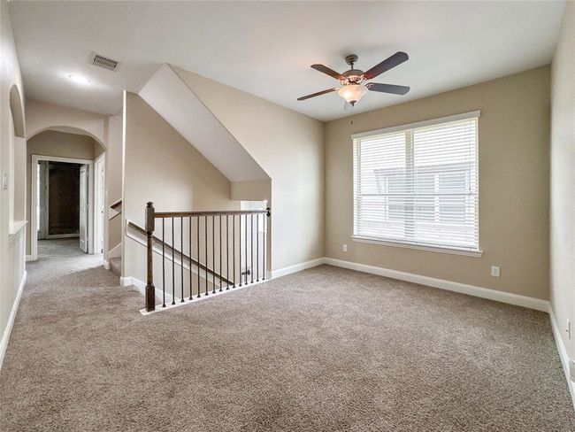 Alternate view of the second floor gameroom with carpeted flooring, a ceiling fan, and a large window for natural light. | Image 14