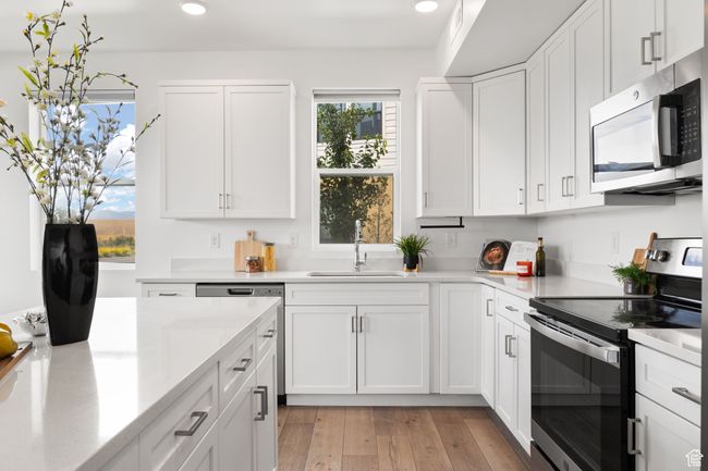 Kitchen with appliances with stainless steel finishes, white cabinets, light wood-style flooring, recessed lighting, and light stone countertops | Image 6
