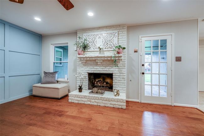 Living Room features a floor-to-ceiling brick fireplace, door out to the covered patio, extensive recessed lighting, ceiling fan, wood floors, and crown molding throughout. | Image 9