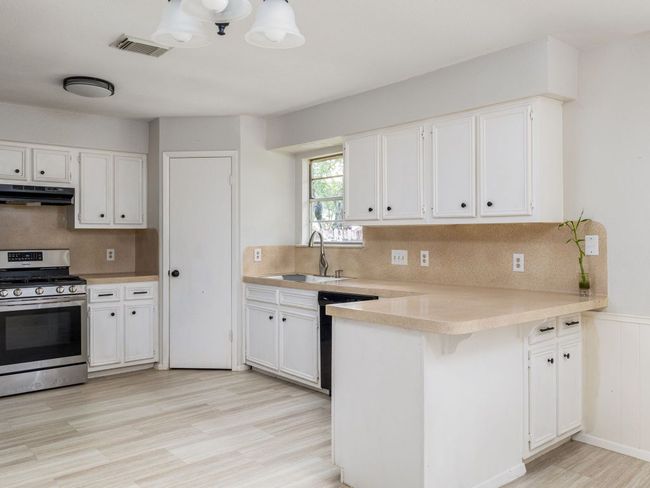 Kitchen with stainless steel gas range oven, under cabinet range hood, a peninsula, black dishwasher, and light countertops | Image 8