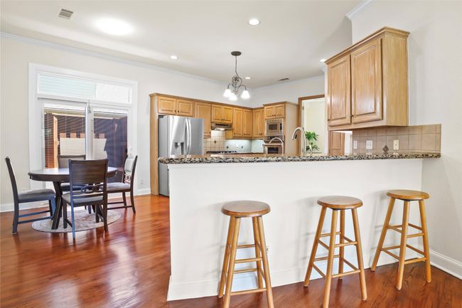Kitchen featuring stainless steel appliances, a peninsula, under cabinet range hood, backsplash, and ornamental molding | Image 9