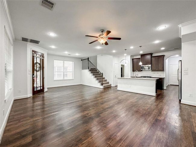 Spacious open-concept living area with luxury vinyl floors, modern kitchen featuring an island and dark cabinetry, ceiling fan, and ample natural light. Includes a staircase leading upstairs, a cozy breakfast nook and welcoming front entry. | Image 5