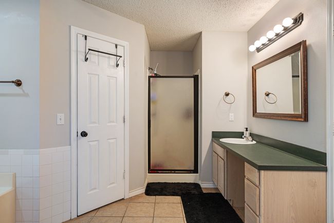 Bathroom featuring a stall shower, tile patterned flooring, vanity, a textured ceiling, and a garden tub | Image 12