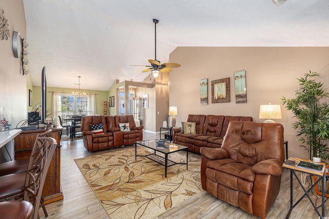 Living area with light wood-style flooring, ceiling fan, vaulted ceiling, a chandelier, and baseboards | Image 11