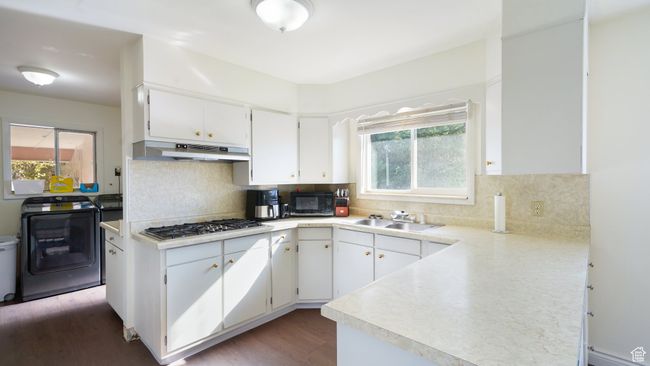 Kitchen featuring washer / clothes dryer, under cabinet range hood, a sink, stainless steel gas stovetop, and black microwave | Image 8
