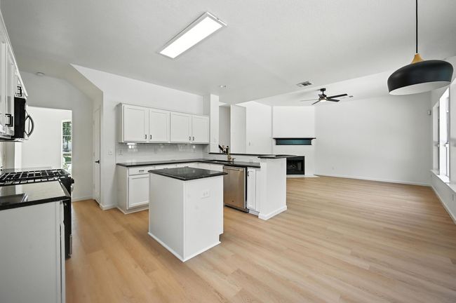 Kitchen featuring a kitchen island, ceiling fan, white cabinets, dark countertops, and decorative backsplash | Image 4