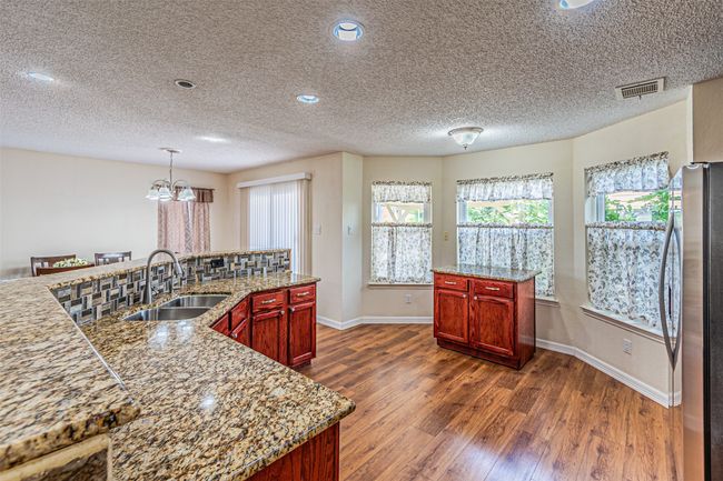Kitchen with freestanding refrigerator, dark wood finished floors, a chandelier, reddish brown cabinets, and a textured ceiling | Image 12