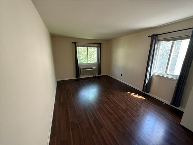 Unfurnished room featuring dark wood-style flooring, a wall unit AC, and baseboards | Image 13