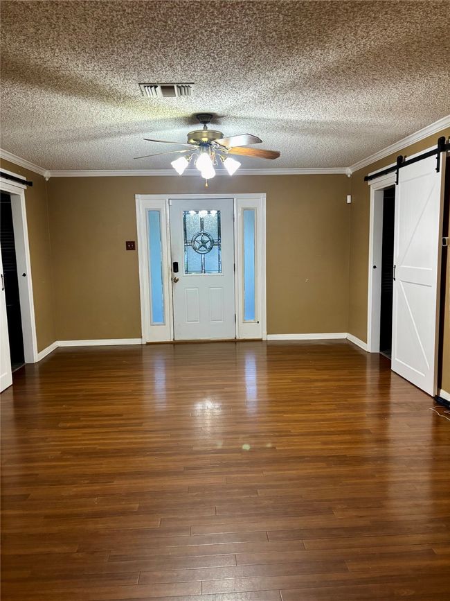 Entryway featuring a barn door, a textured ceiling, ceiling fan, ornamental molding, and wood finished​​‌​​​​‌​​‌‌​‌‌​​​‌‌​​‌‌​‌​​​​​‌ floors | Image 4