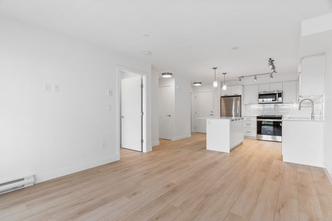 Unfurnished living room with a sink, a baseboard heating unit, light wood-style floors, track lighting, and baseboards | Image 11