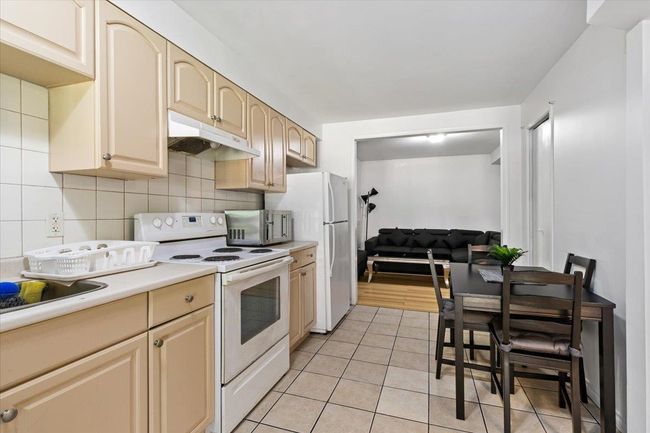 Kitchen featuring white appliances, light tile patterned floors, decorative backsplash, light countertops, and under cabinet range hood | Image 27