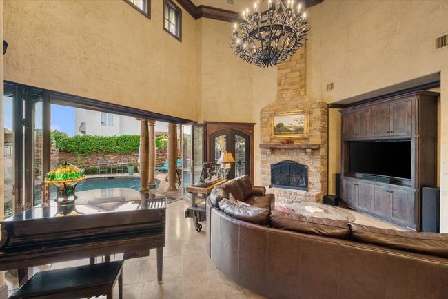 Living room featuring a high ceiling, a chandelier, a stone fireplace, ornamental molding, and travertine flooring | Image 7
