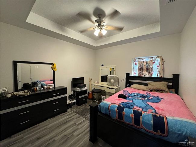 Bedroom with a tray ceiling, dark wood-style floors, and ceiling fan | Image 4