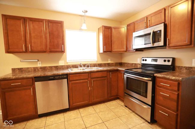 kitchen with light tile patterned floors, decorative light fixtures, appliances with stainless steel finishes, dark countertops, and a sink | Image 20