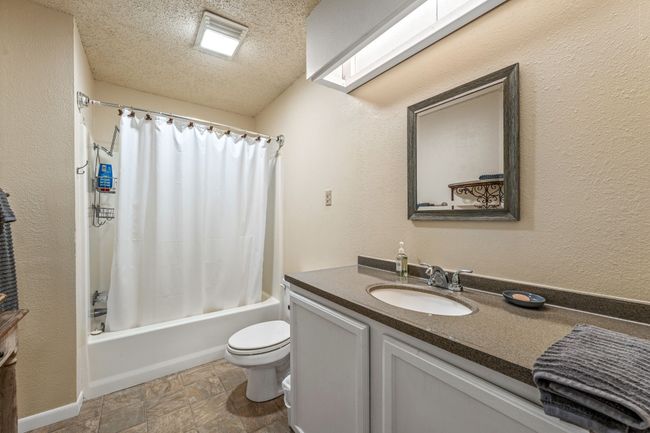 Full bathroom with shower / tub combo, vanity, a textured ceiling, toilet, and stone finish flooring | Image 15