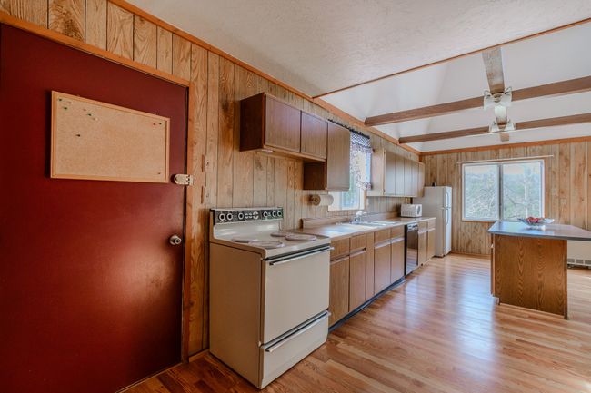 Kitchen with wood walls, a kitchen island, beam ceiling, light wood-type flooring, and white appliances | Image 31