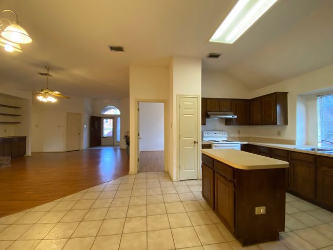 Kitchen with white electric stove, under cabinet range hood, lofted ceiling, a center island, and light countertops | Image 10