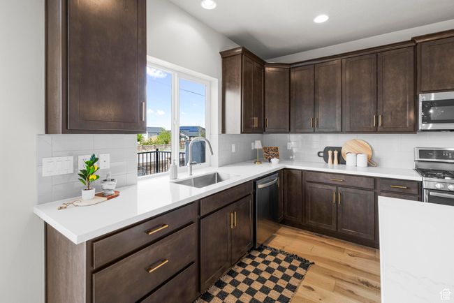 Kitchen with a sink, stainless steel appliances, light wood-type flooring, light countertops, and dark brown cabinets | Image 11