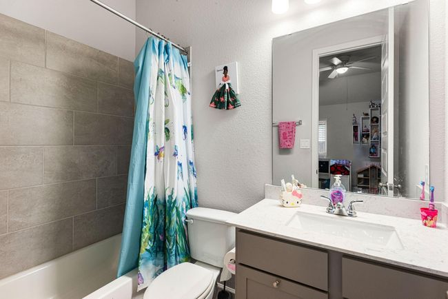Secondary bathroom features light countertops and dark cabinets, neutral paint, shower/tub combo with tile surround, large mirror, tile floors and plenty of space to accommodate any visiting family or guests. | Image 14