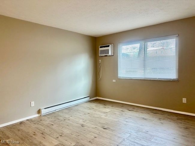 Unfurnished room featuring a textured ceiling, wood finished floors, a wall unit AC, a baseboard radiator, and baseboards | Image 16