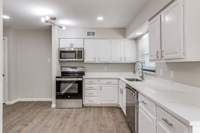 Kitchen with appliances with stainless steel finishes, light wood finished floors, white cabinets, and recessed lighting | Image 13