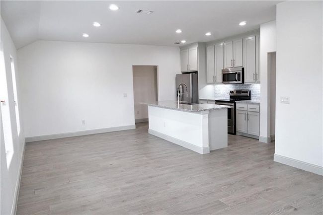 Kitchen featuring stainless steel appliances, an island with sink, backsplash, light wood finished floors, and recessed lighting | Image 5