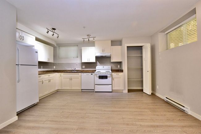 Kitchen featuring white appliances, a baseboard heating unit, under cabinet range hood, and dark countertops | Image 31