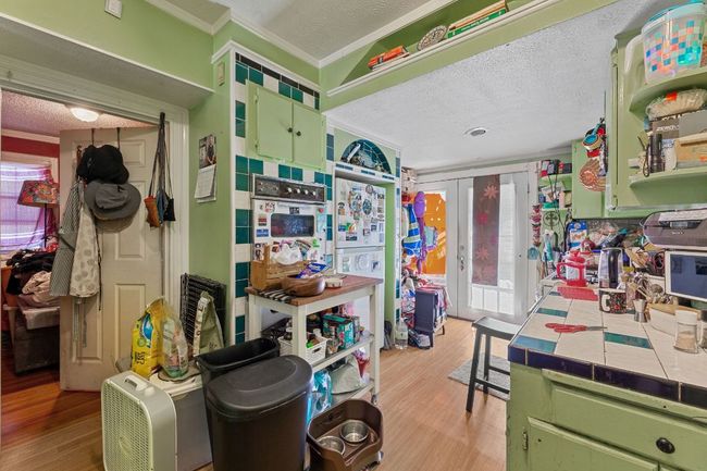 Kitchen featuring crown molding, tile counters, light wood-style floors, a textured ceiling, and green cabinetry | Image 17