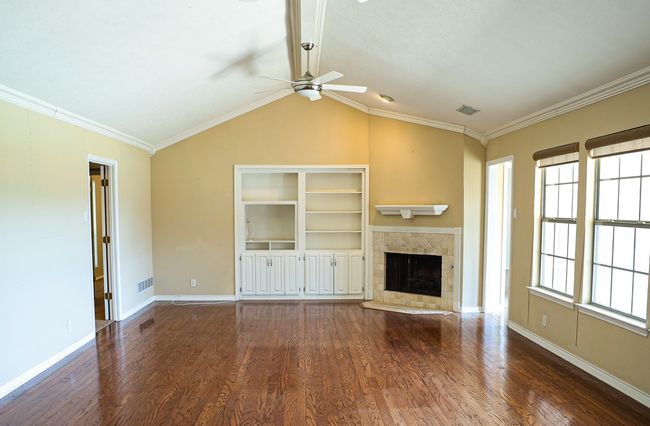 Unfurnished living room with a ceiling fan, wood finished floors, a tiled fireplace, vaulted ceiling, and crown molding | Image 12