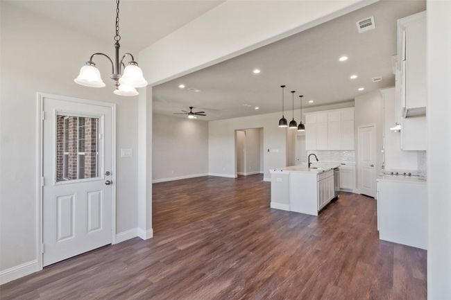 Kitchen with ceiling fan with notable chandelier, white cabinets, a sink, open floor plan, and a center island with sink | Image 6