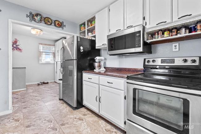 Kitchen featuring appliances with stainless steel finishes, open shelves, white cabinets, and dark countertops | Image 16