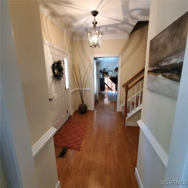 Hall with visible vents, a notable chandelier, wood finished floors, crown molding, and stairs | Image 17