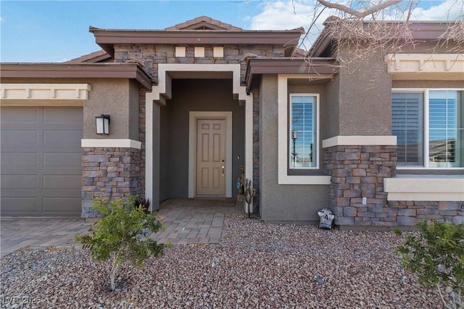 View of exterior entry with stone siding, an attached garage, a tile roof, and stucco siding | Image 8