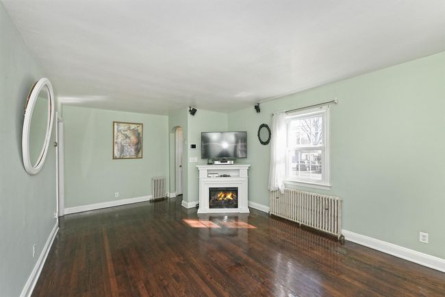 Unfurnished living room featuring arched walkways, wood finished floors, radiator heating unit, and a glass covered fireplace | Image 5