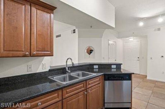 Kitchen with light tile patterned floors, a sink, a peninsula, dark stone counters, and stainless steel dishwasher | Image 14