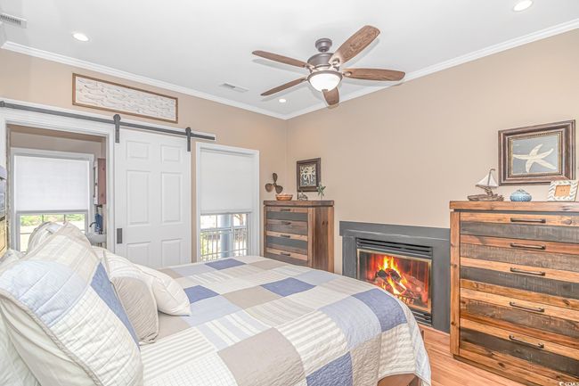 Bedroom featuring a barn door, crown molding, a glass covered fireplace, light wood finished floors, and recessed lighting | Image 16