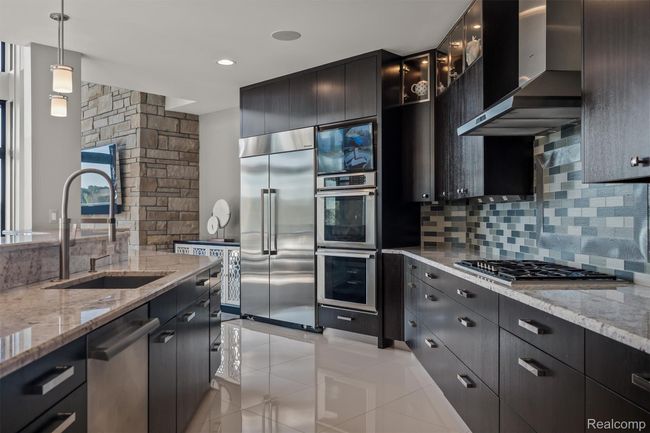 Kitchen with light stone countertops, hanging light fixtures, dark cabinetry, appliances with stainless steel finishes, and tasteful backsplash | Image 13