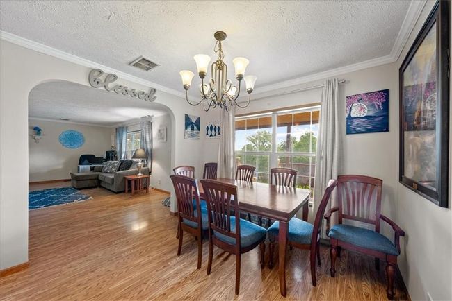 Dining area featuring light wood-type flooring, an inviting chandelier, ornamental molding, a textured ceiling, and arched walkways | Image 13