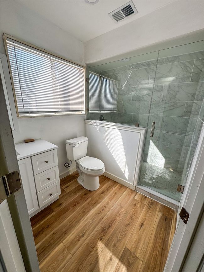 Bathroom with a shower stall, toilet, wood finished floors, and visible vents | Image 20