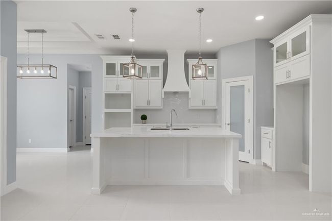 Kitchen featuring premium range hood, a kitchen island with sink, light countertops, decorative backsplash, and white cabinetry | Image 4