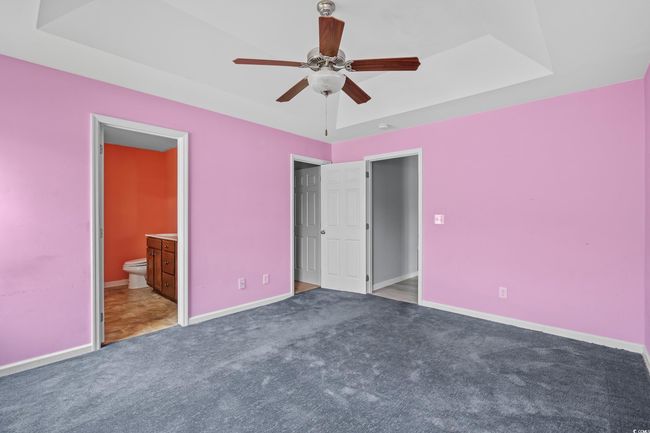 Unfurnished bedroom featuring a tray ceiling, carpet floors, ensuite bathroom, baseboards, and a ceiling fan | Image 29