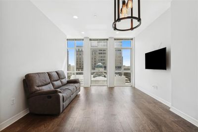 Living room featuring an open dining area with contemporary lighting feature accents the rich wood flooring throughout the condo ! | Image 3