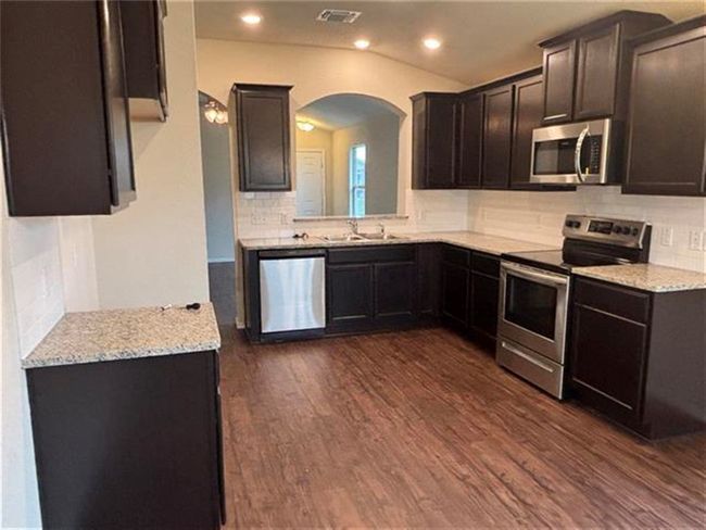 Kitchen with appliances with stainless steel finishes, arched walkways, tasteful backsplash, dark wood-style floors, and light stone countertops | Image 4