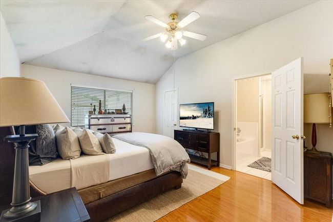 Cozy bedroom with warm laminate flooring, vaulted ceiling, and ceiling fan. Features a large window for natural light, a comfortable bed, and an ensuite bathroom. | Image 15