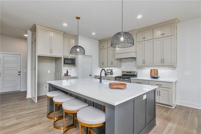 Kitchen with tasteful backsplash, gas stove, premium range hood, light wood-type flooring, and an island with sink | Image 12