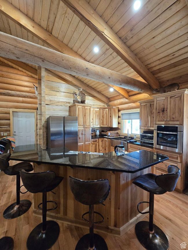 Kitchen with a breakfast bar, appliances with stainless steel finishes, log walls, and light wood-type flooring | Image 55